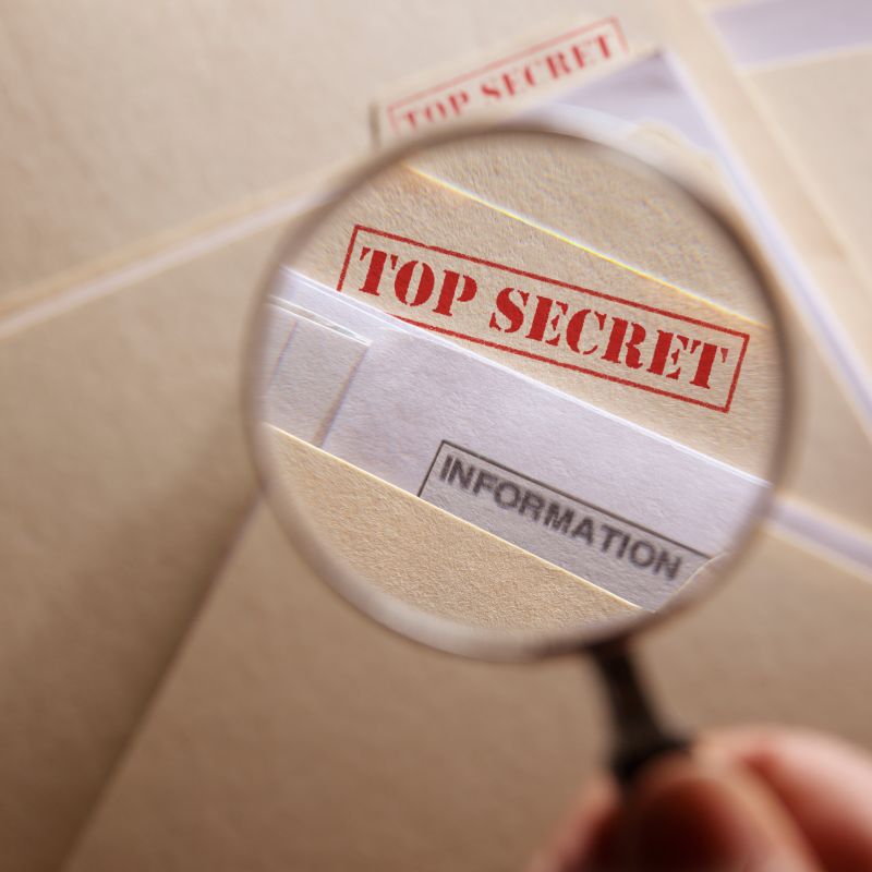 A magnifying glass is held over a folder labeled top secret information.