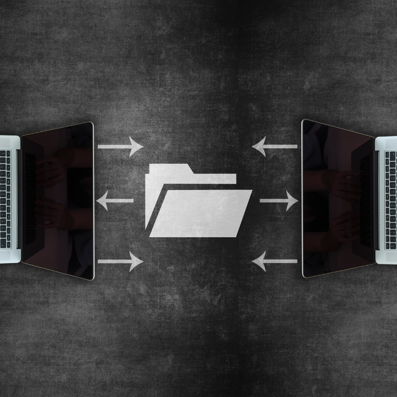 Two laptops face one another with an image of a folder and arrows passing through it between them.