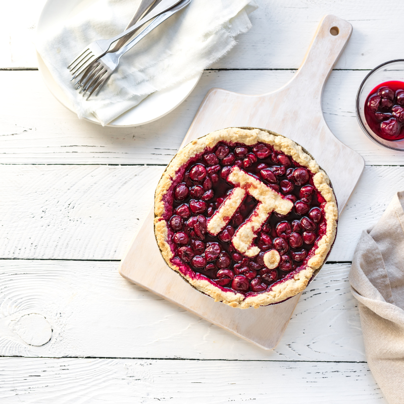 A table with silverware and a pie on it. The pie has the crust shaped into the symbol for the mathematical pi.