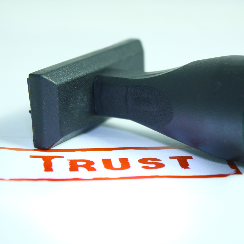A stamper lays on a table next to the ink stamp of the word TRUST