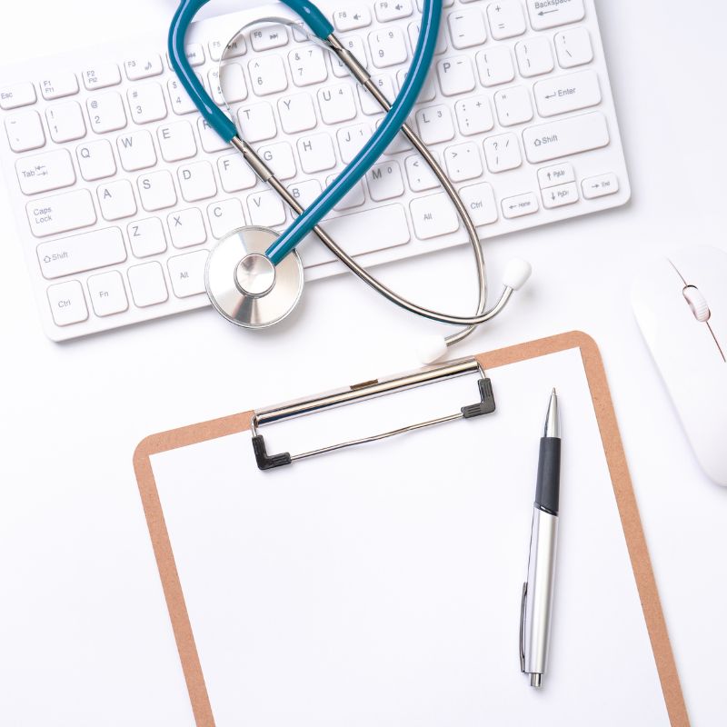 A stethoscope sits on top of a keyboard in front of a blank clipboard.