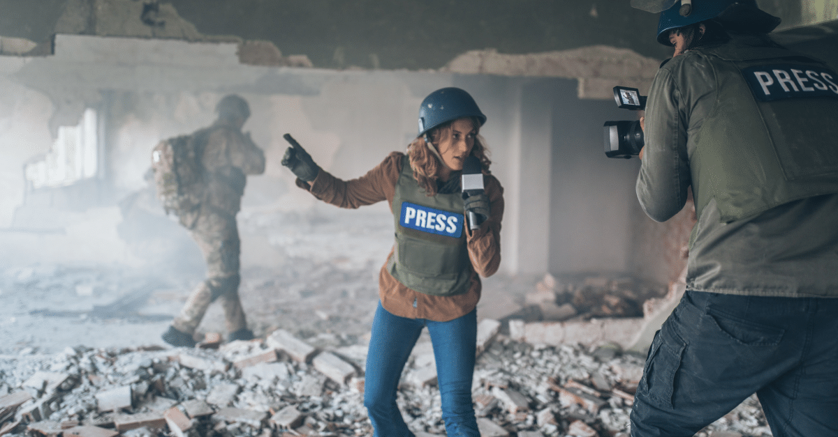 Female reporter wearing Press protective gear and helmet reports from a battle zone