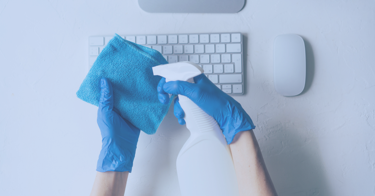 Person wearing blue rubber gloves holding blue cloth and spray bottle to clean computer keyboard - Votiro